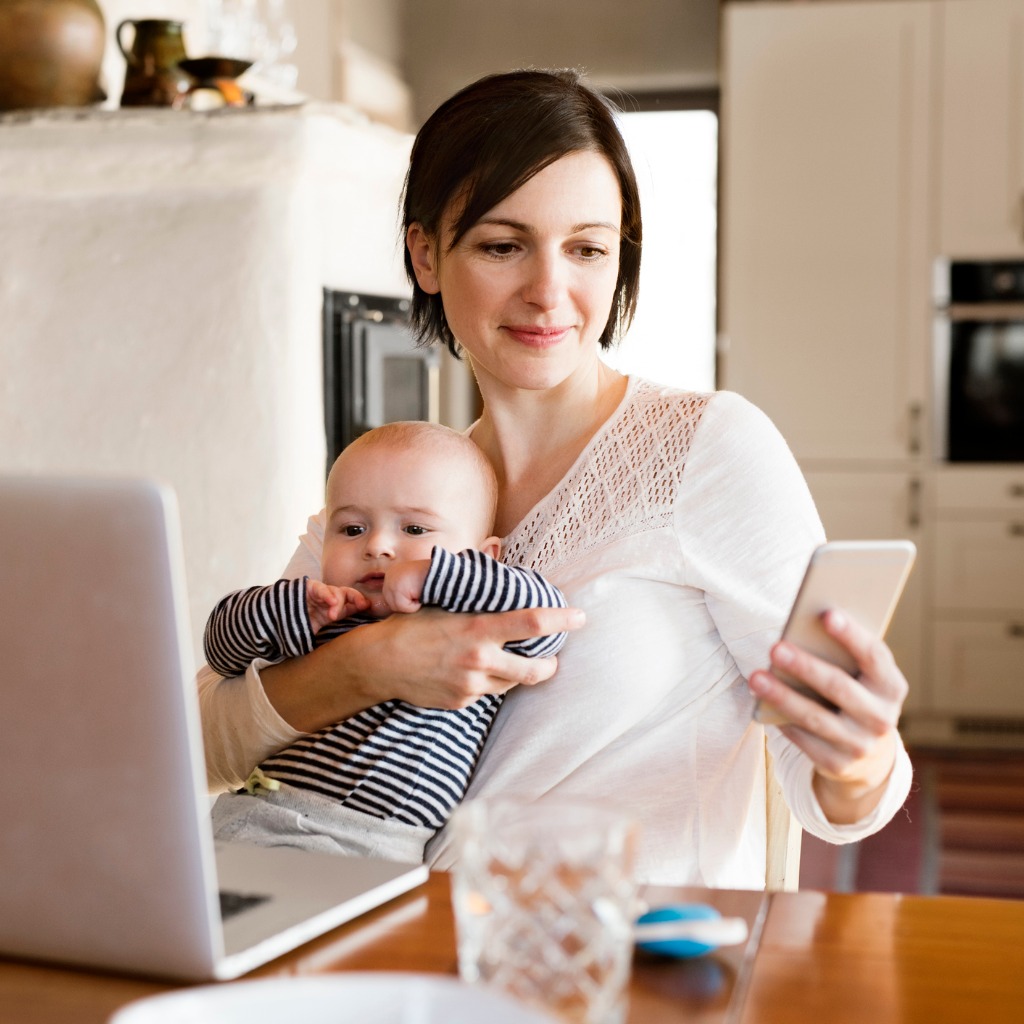 mother at home with baby working on laptop holding smartphone picture id646958030