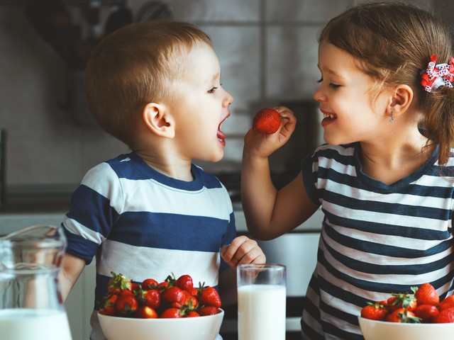 Happy children girl and boy brother and sister eating strawberries with milk