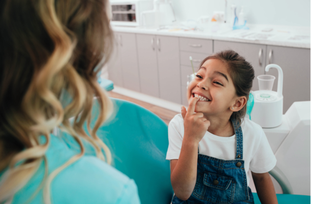 Mixed race little patient showing her perfect toothy smile while sitting dentists chair