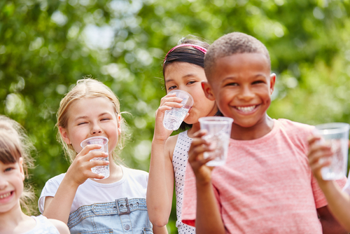 Children with plastic cups drinking water in summer in the park