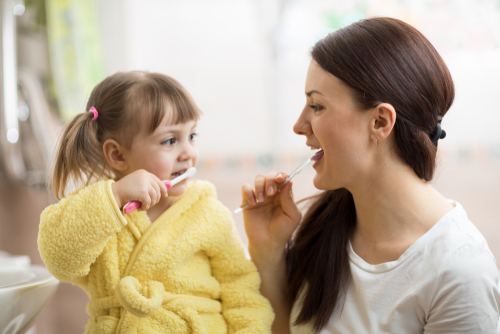 mom teaching daughter child teeth brushing in bathroom