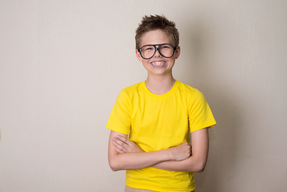 Happy young boy with glasses smiling confidently, showing children's permanent teeth and dental health